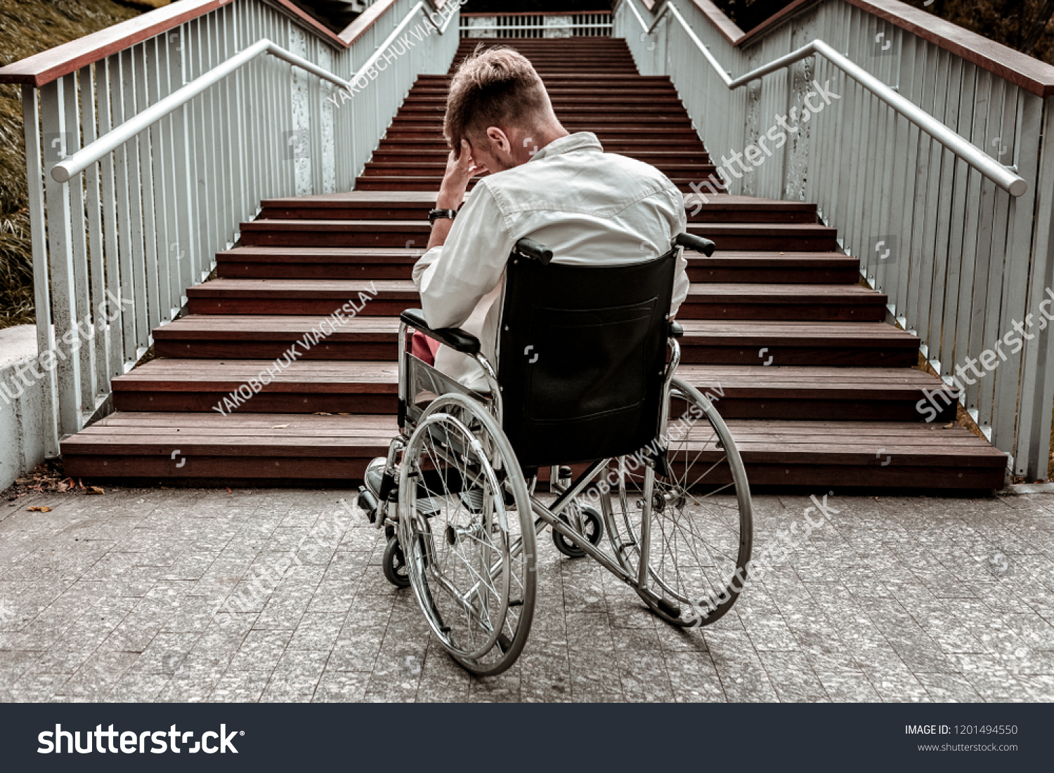 Many stairs. Horizontal image of depressed disabled man sitting in the wheelchair and facing the difficulties with climbing the stairs alone #1201494550