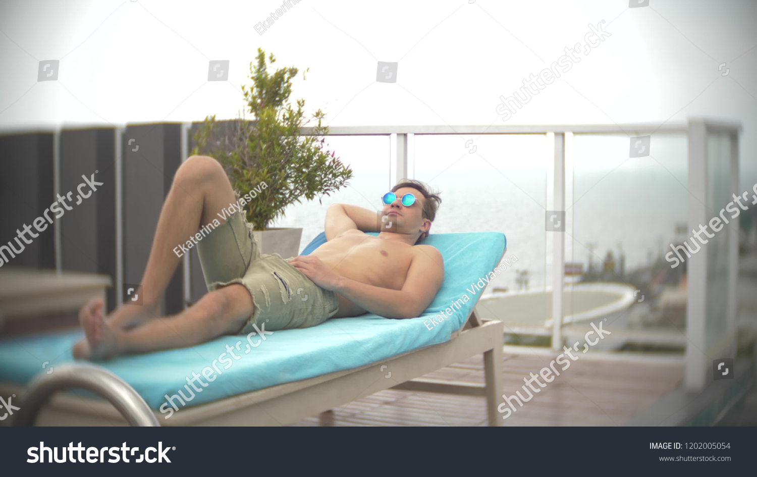 A man relaxing, sunbathing on the loungers near the pool on the roof overlooking the sea. background blur #1202005054