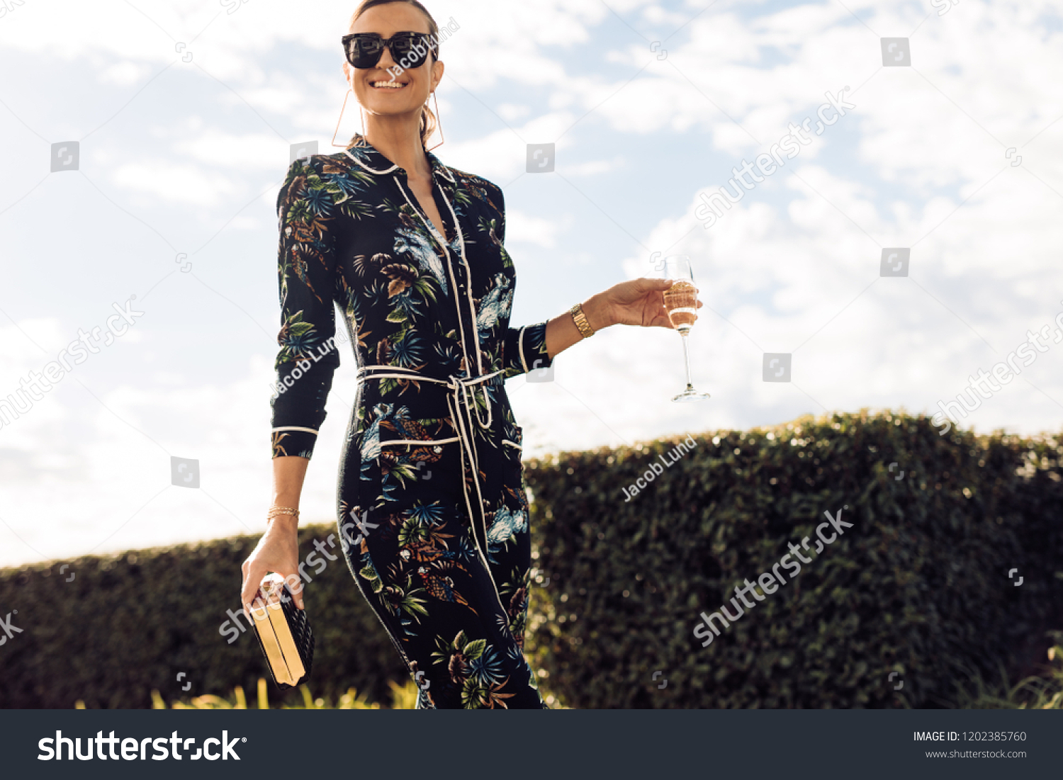 Stylish young woman walking with glass of wine. Wealthy female with wine walking outdoors. #1202385760