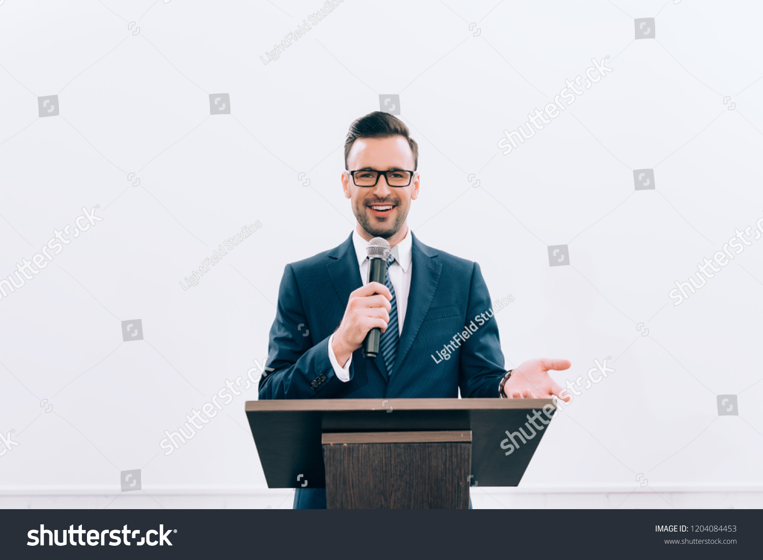 smiling speaker gesturing and talking into microphone at podium tribune during seminar in conference hall #1204084453