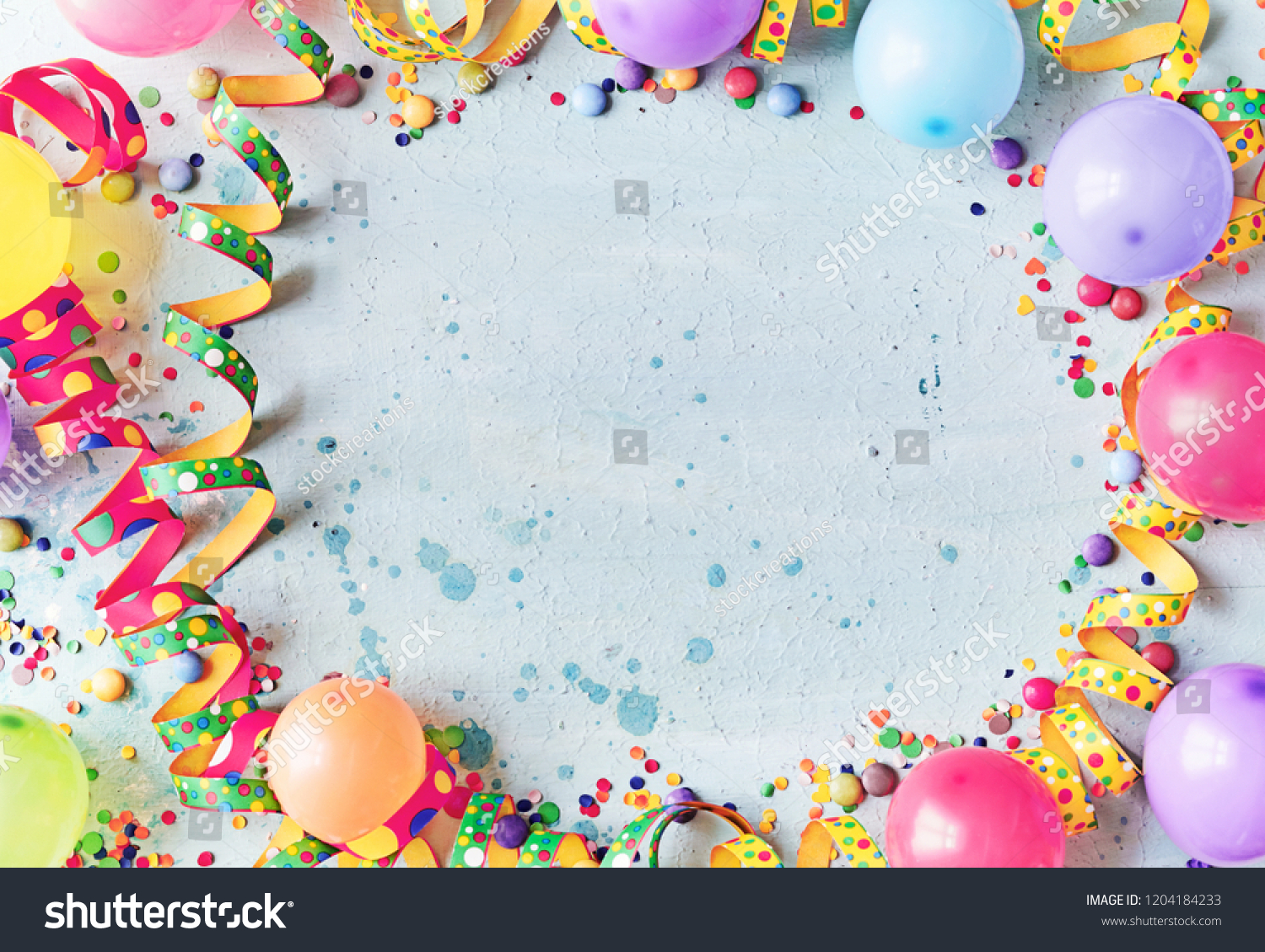 Multicolored carnival or birthday background on blue with a frame of colorful party balloons, streamers, confetti and candy around central copy space #1204184233