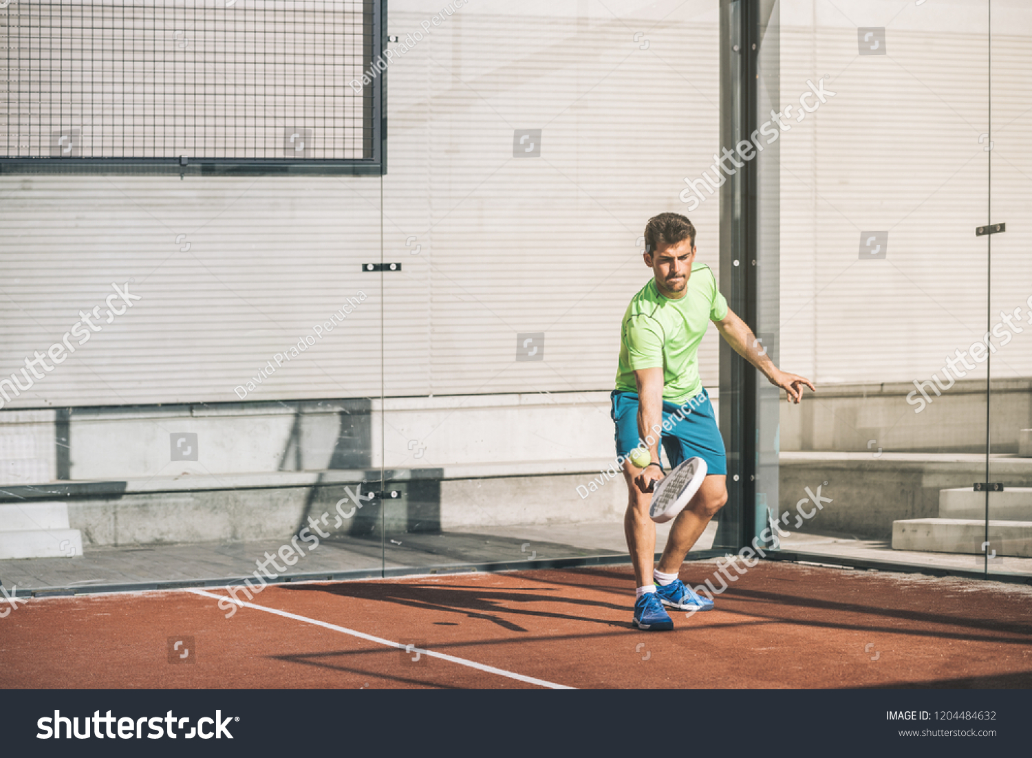 Man playing padel in a orange grass padel court outdoors behind the net #1204484632