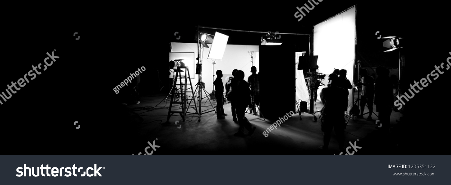 Silhouette images of video production behind the scenes or b-roll or making of TV commercial movie that film crew team lightman and cameraman working together with director in big studio  #1205351122