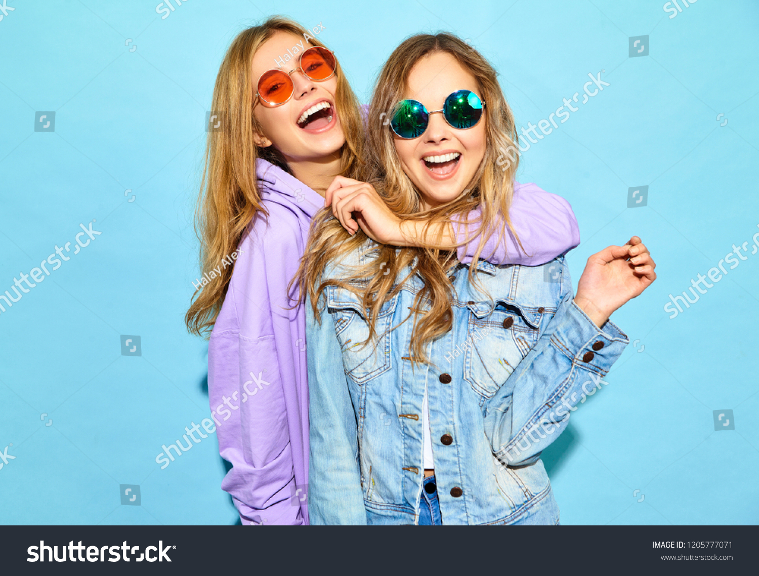 Two young beautiful blond smiling hipster girls in trendy summer clothes. Sexy carefree women posing near blue wall in sunglasses. Positive models going crazy #1205777071