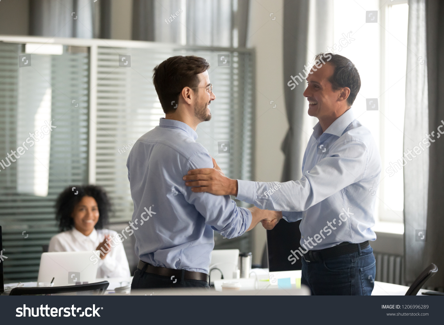 Smiling middle-aged ceo promoting motivating worker shaking hands congratulating with achievement promising respect bonus thanking for good work, team applauding, employee reward recognition concept #1206996289