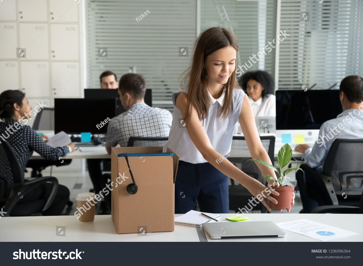 Smiling hired female company employee unpacking box with personal belongings at workplace on first working day in shared office, happy intern or newcomer got new job excited to start work concept #1206996364