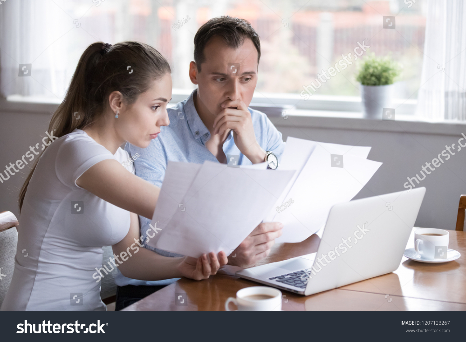 Stressed millennial married couple sitting at the desk at home use laptop checking documents unpaid bills, taxes, due debt, bank account balance. Bankruptcy lack of money financial problems concept #1207123267