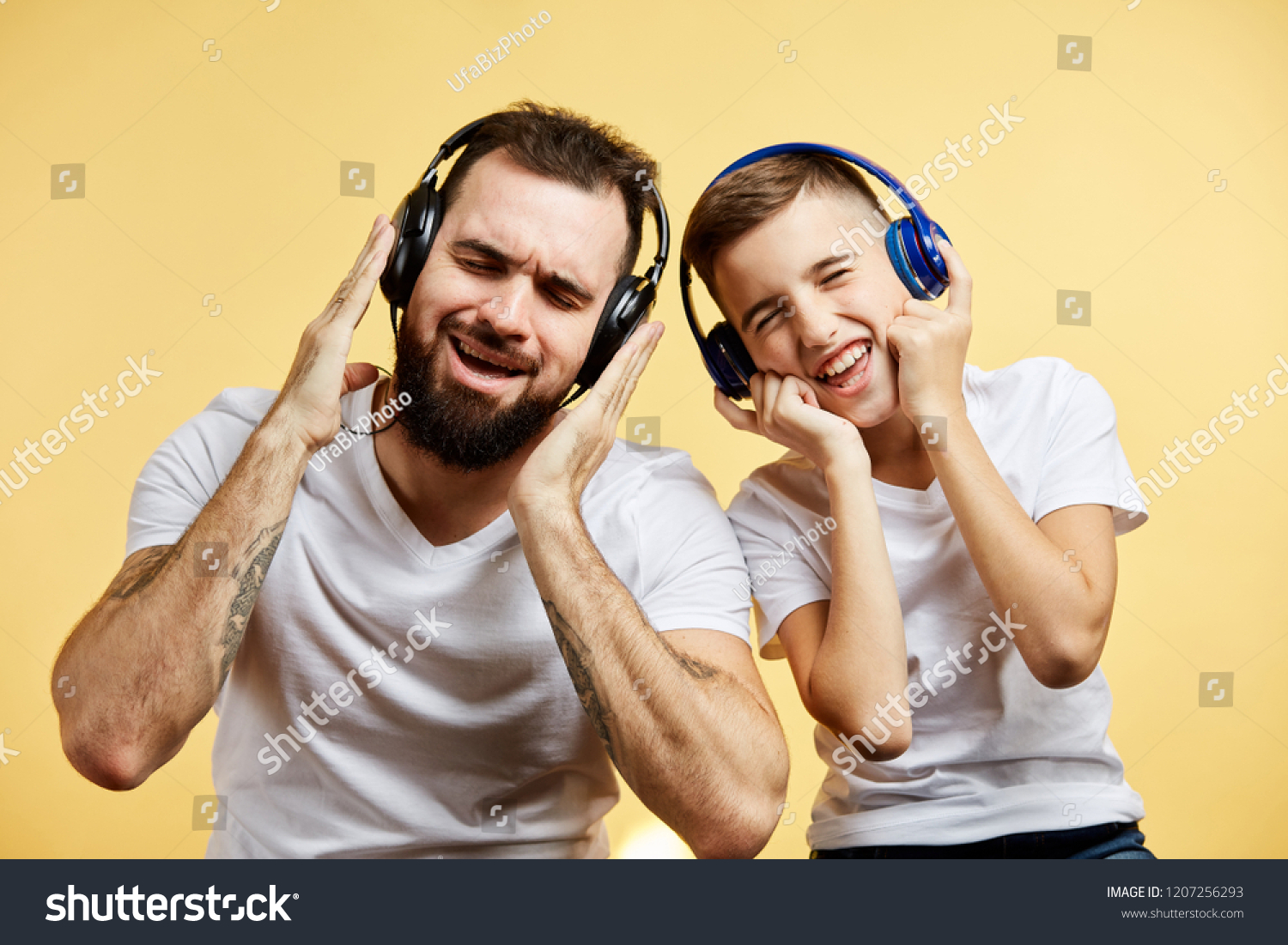 Bearded father and his son in headphones listen to music on yellow background #1207256293