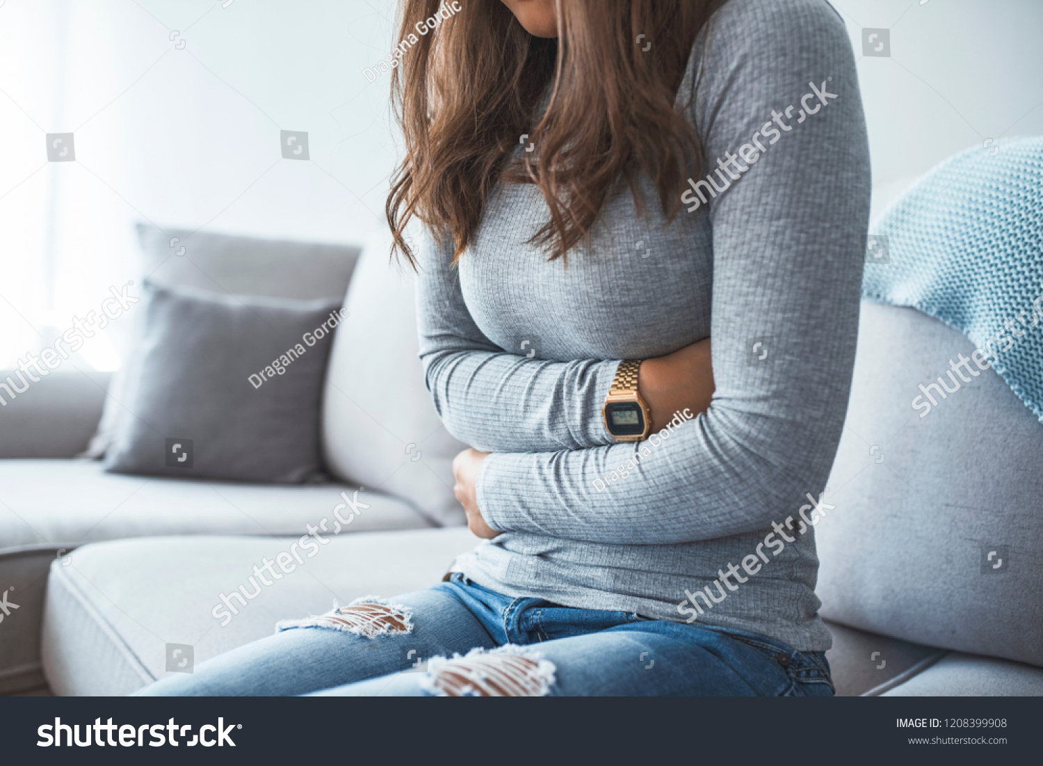 Woman lying on sofa looking sick in the living room. Beautiful young woman lying on bed and holding hands on her stomach. Woman having painful stomachache on bed, Menstrual period #1208399908
