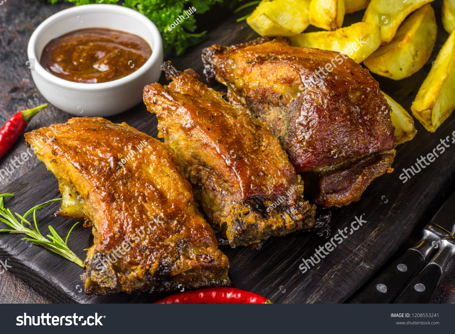 Barbecued pork ribs seasoned with a spicy bbq sauce served with fries on an old rustic wooden chopping board in a country kitchen #1208553241