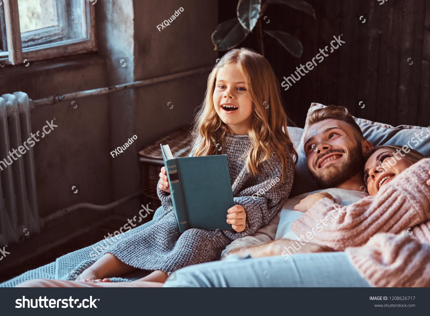 Mom, dad and daughter reading storybook together while lying on bed. #1208626717