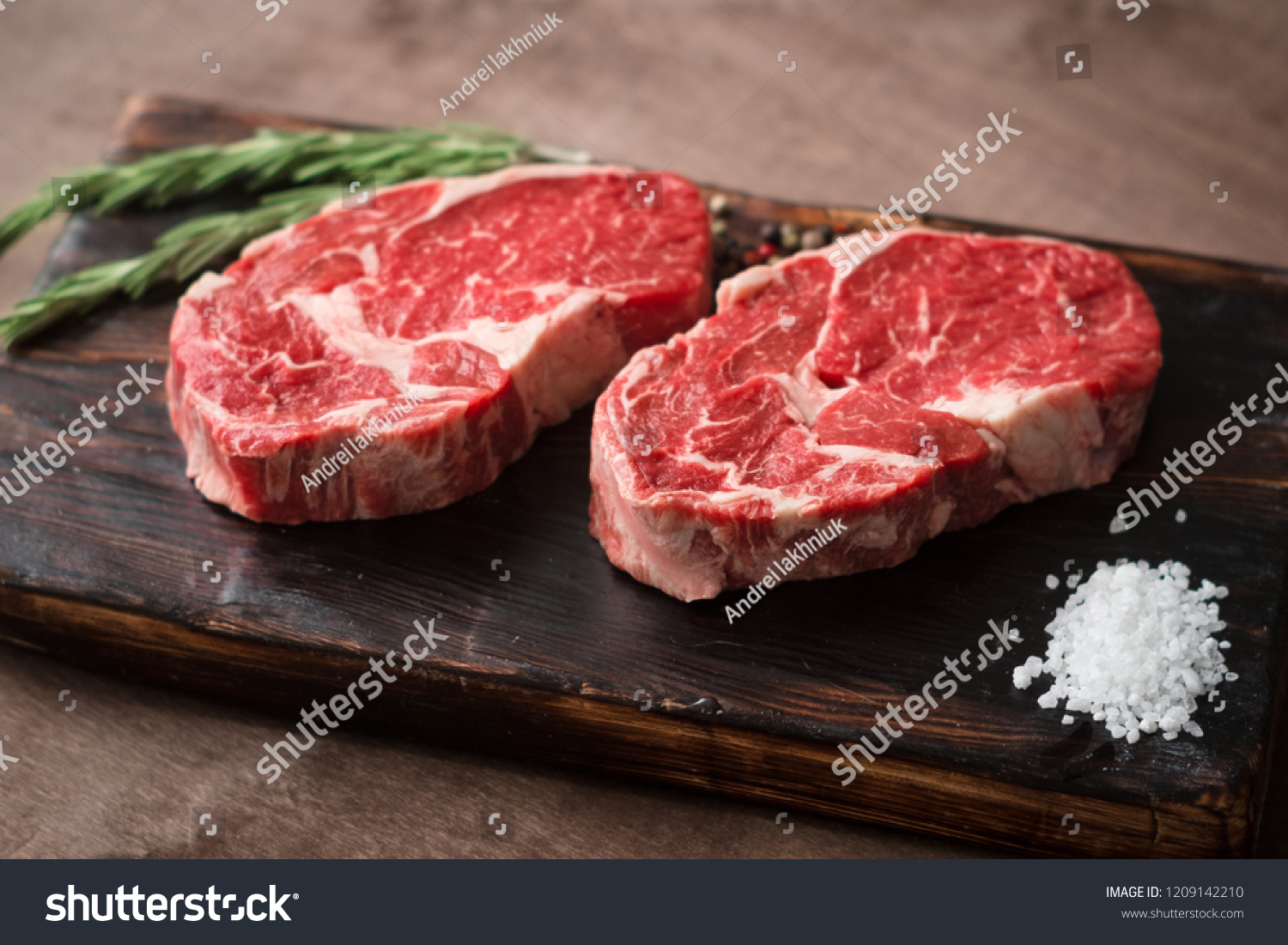 Two fresh raw rib-eye steak on wooden Board on wooden background with salt, pepper and rosmary in a rustic style #1209142210