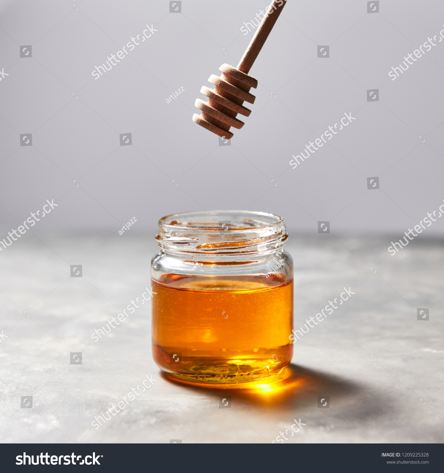 Wooden stick above a glass jar with aromatic natural organic honey on a gray concrete table, place for text. Jewish New Year healthy holiday concept. Traditional useful sweetness. #1209225328