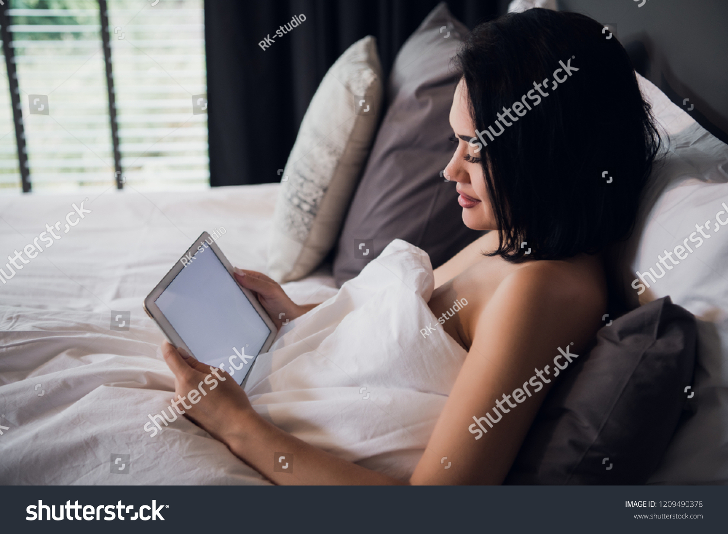 Young woman enjoying en e-book as she relaxes in the bed with tablet pc #1209490378