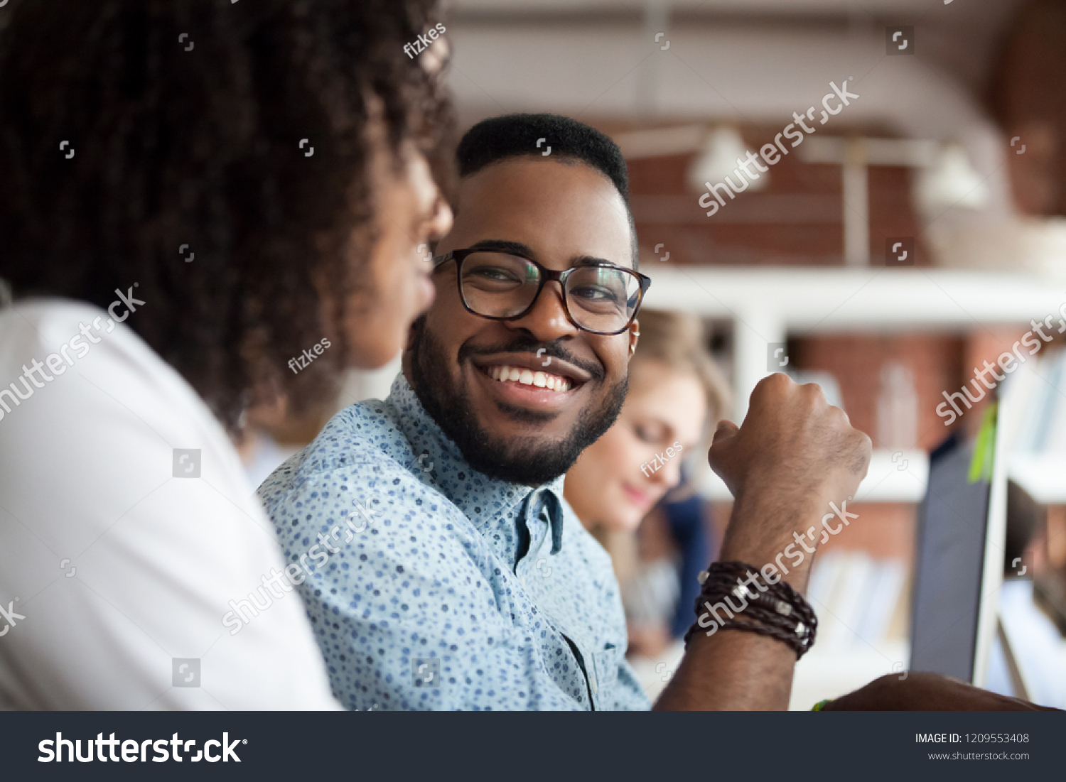 Close up of smiling African American employee look at female colleague chatting in office, happy black male worker talk with woman coworker, having casual conversation at workplace, have fun #1209553408