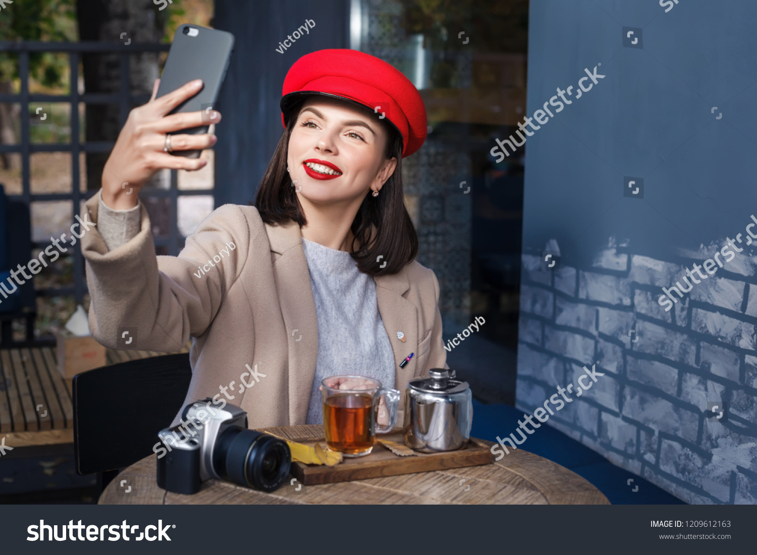 Young smiling woman drinking tea in a cafe and making selfie #1209612163