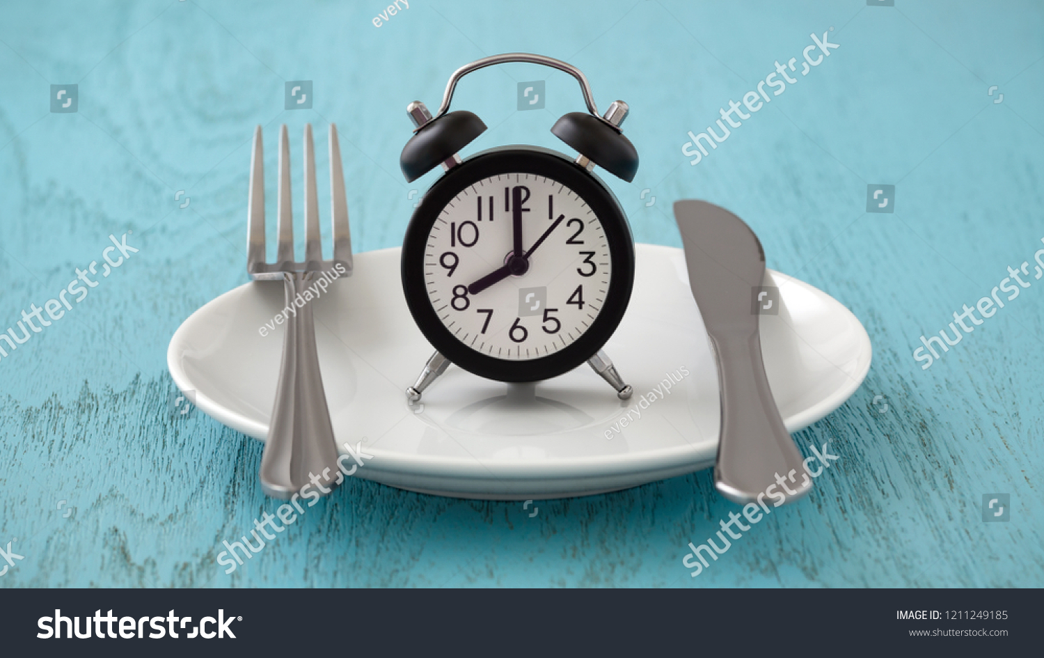 Clock on white plate with fork and knife, intermittent fasting, meal plan, weight loss concept on blue table #1211249185