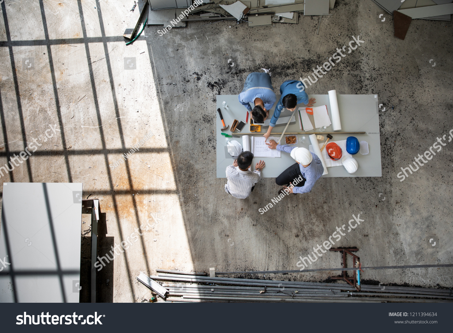 Four persons professional team of engineers talk together to review material in construction site, taken from above high angle, top view photo with shadow of window frame on floor. #1211394634