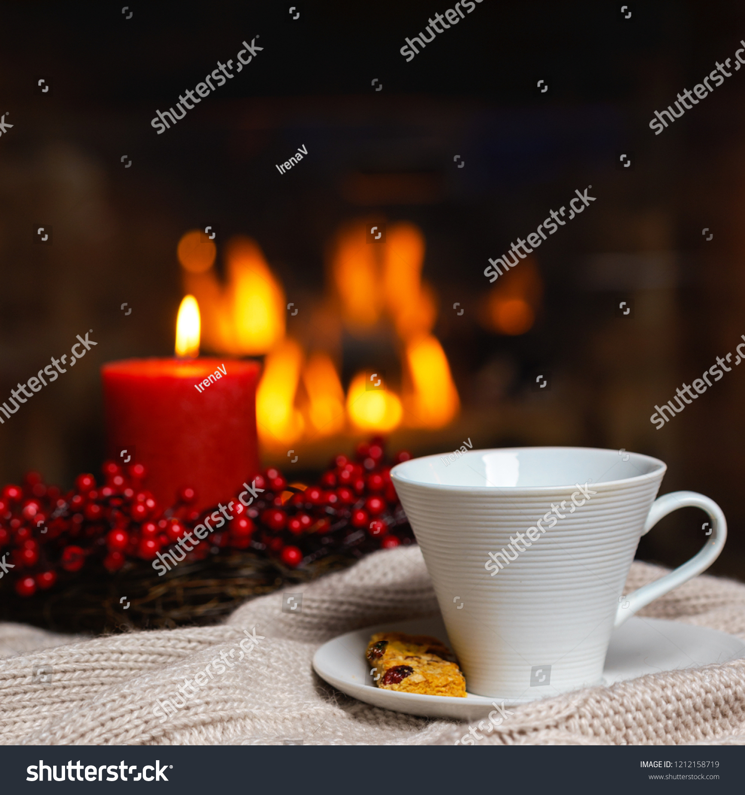 Cup of hot drink with cookie berries and red candle in red Christmas decoration on cozy knitted plaid in front of fireplace. Christmas New Year concept. Cozy relaxed magical atmosphere home interior. #1212158719