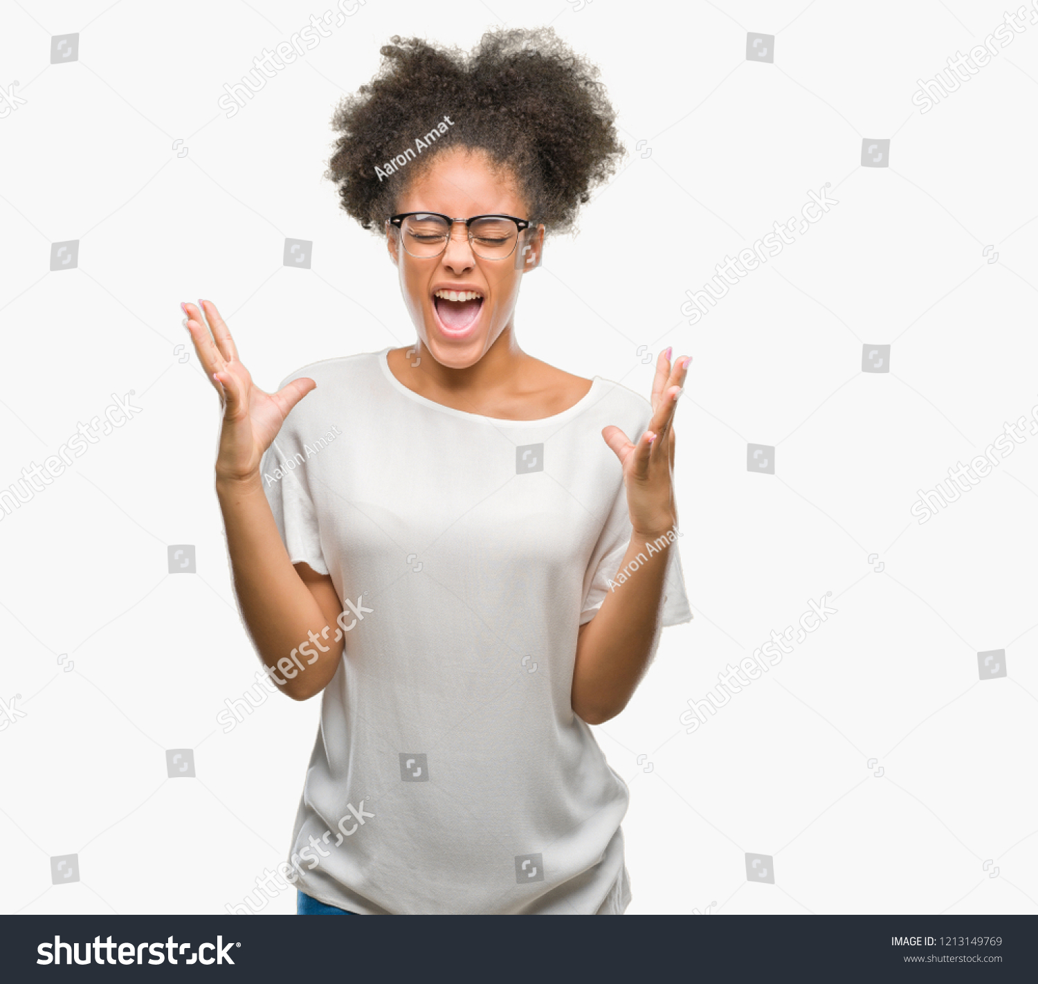 Young afro american woman wearing glasses over isolated background celebrating mad and crazy for success with arms raised and closed eyes screaming excited. Winner concept #1213149769
