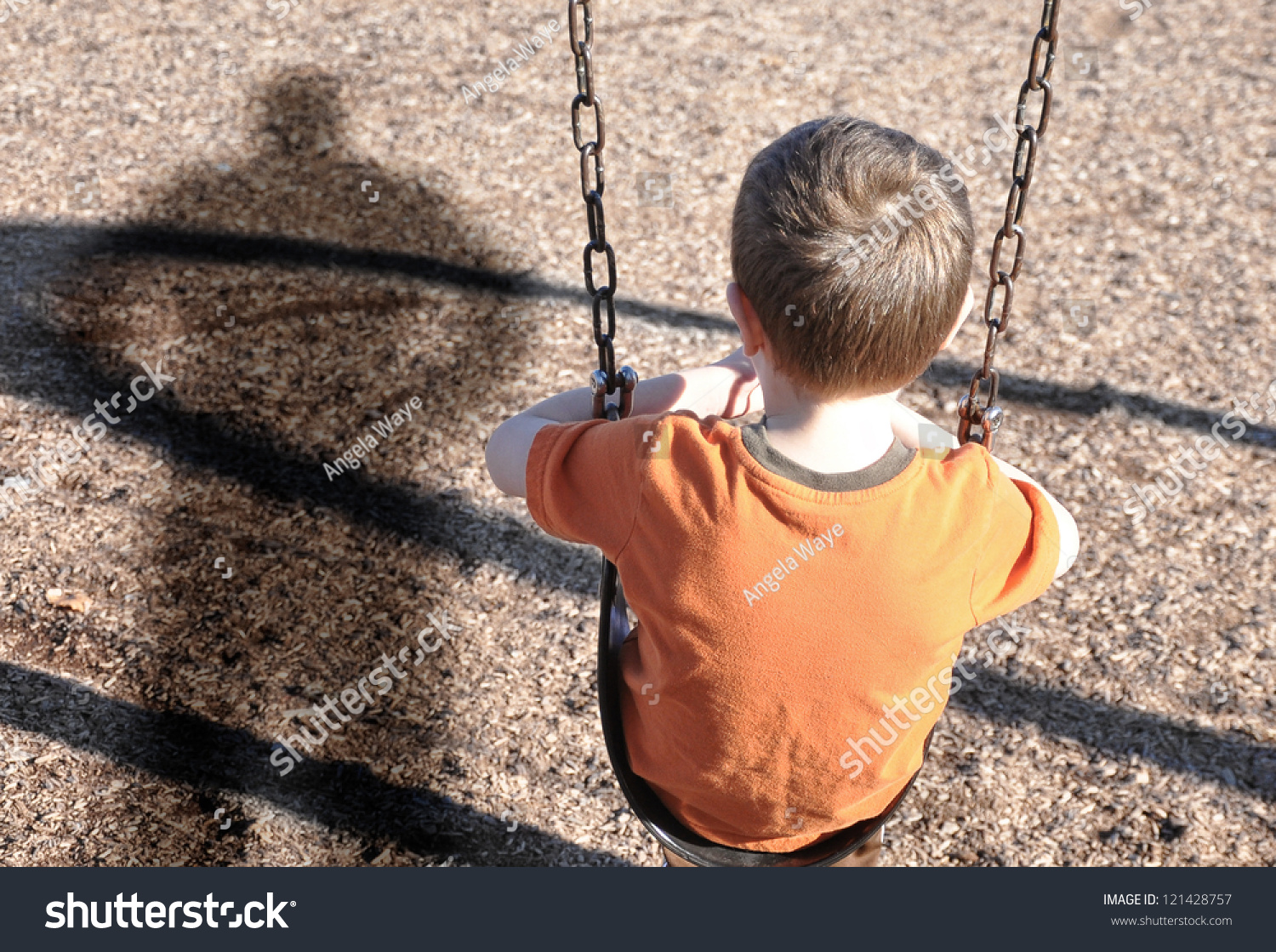 A young boy is sitting on a swing set and looking at a shadow figure of a man or bully at a playground. Use it for a kidnap, defense or safety concept. #121428757