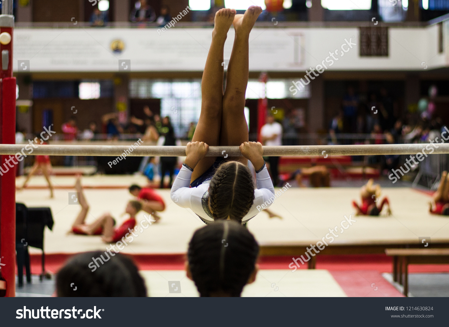 Athletic little girl gymnast performing exercises at the bar in the championship #1214630824