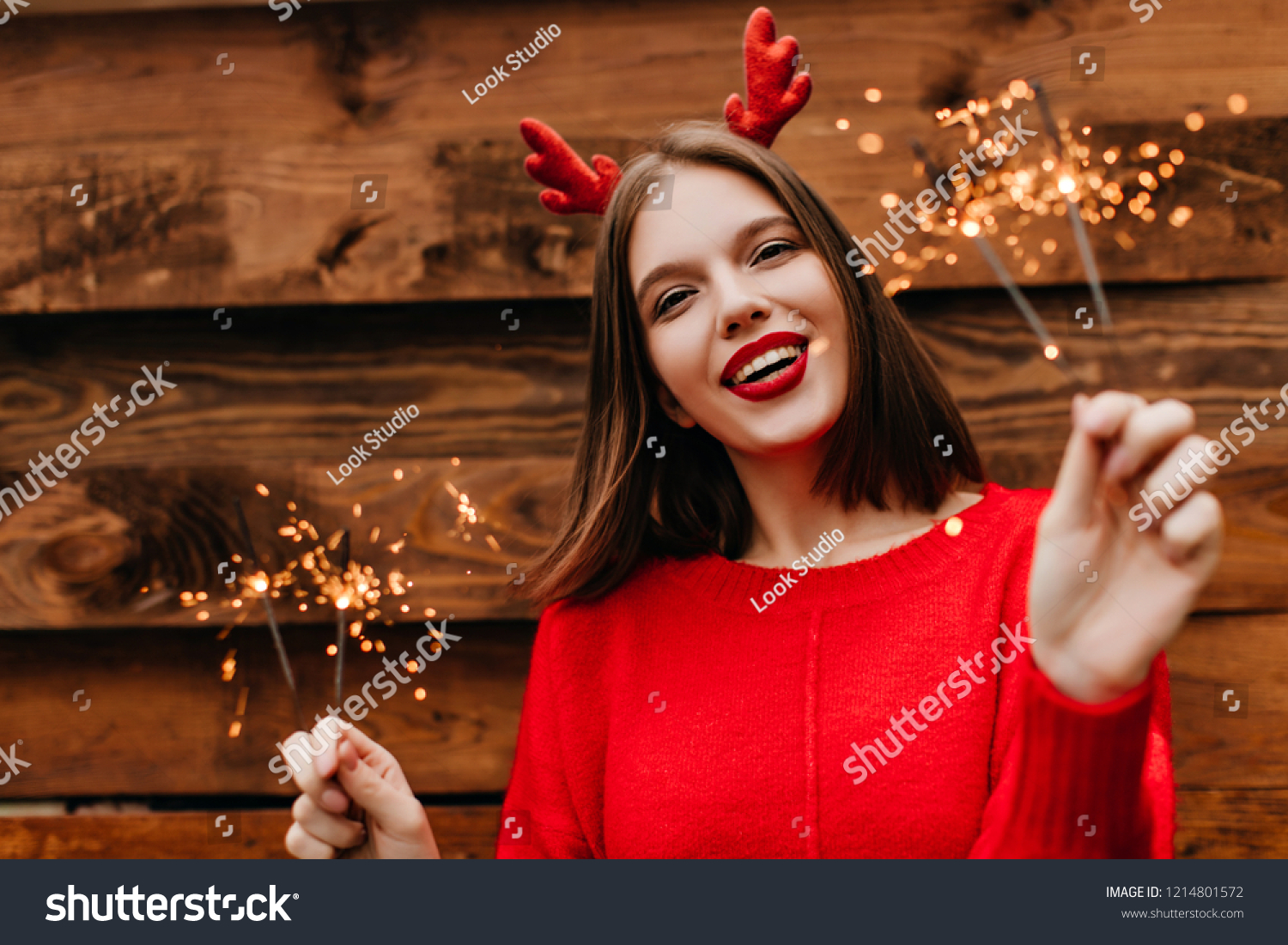 Lovely female model with straight hairstyle holding bengal lights with inspired smile. Cute woman in red sweater preapring for new year. #1214801572