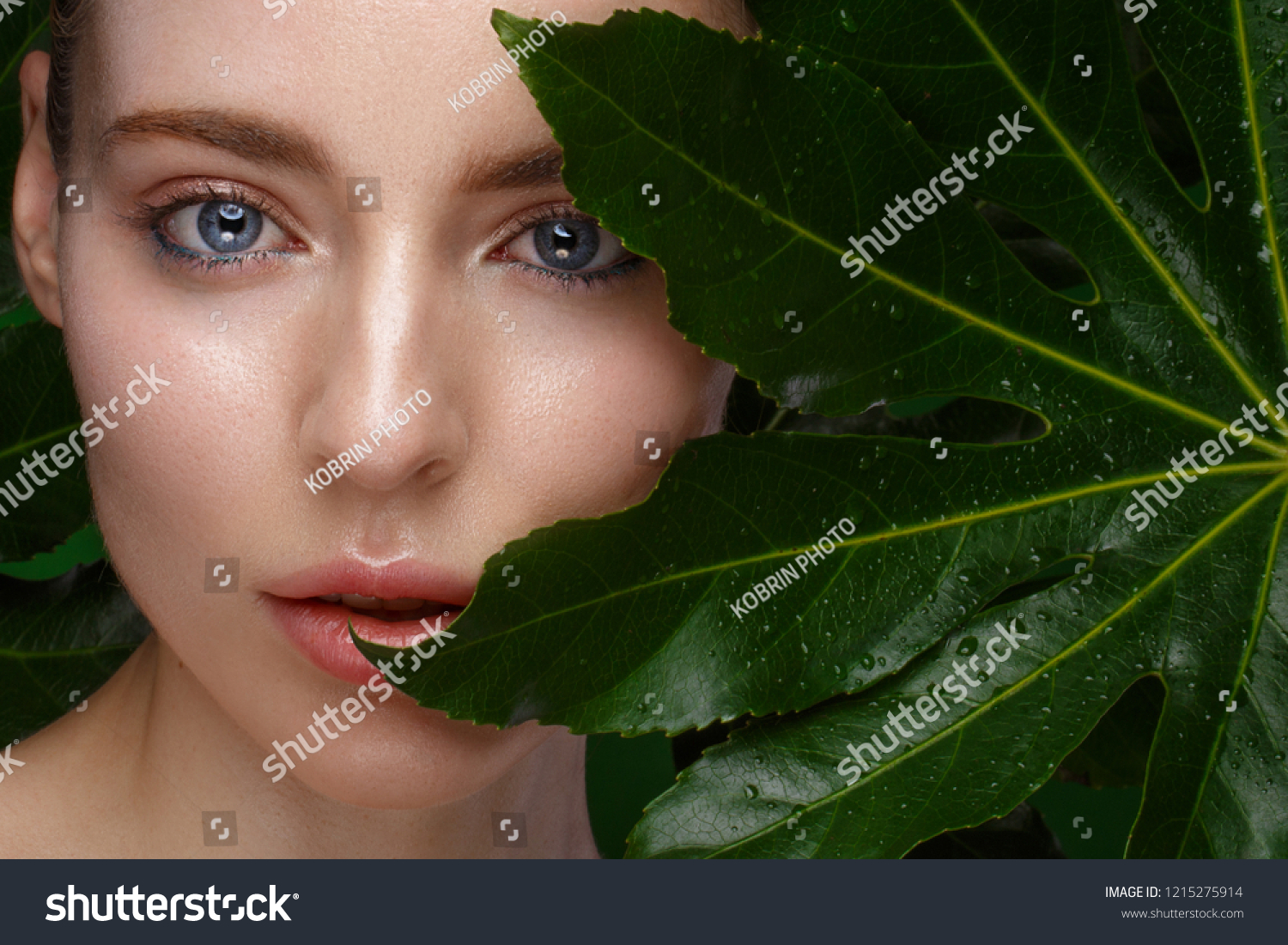 Beautiful fresh girl with perfect skin, natural make-up and green leaves. Beauty face. Photo taken in the studio. #1215275914
