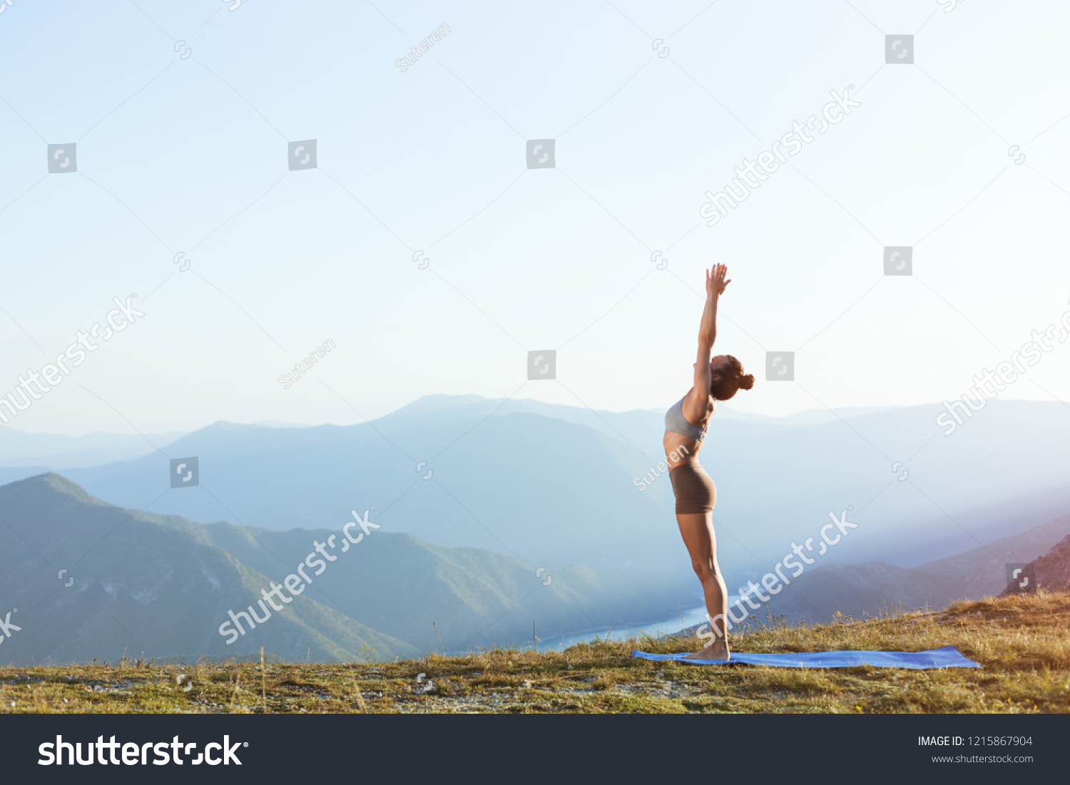 Female practicing sun salutation and doing morning yoga on top of a mountain in peaceful and quiet environment #1215867904