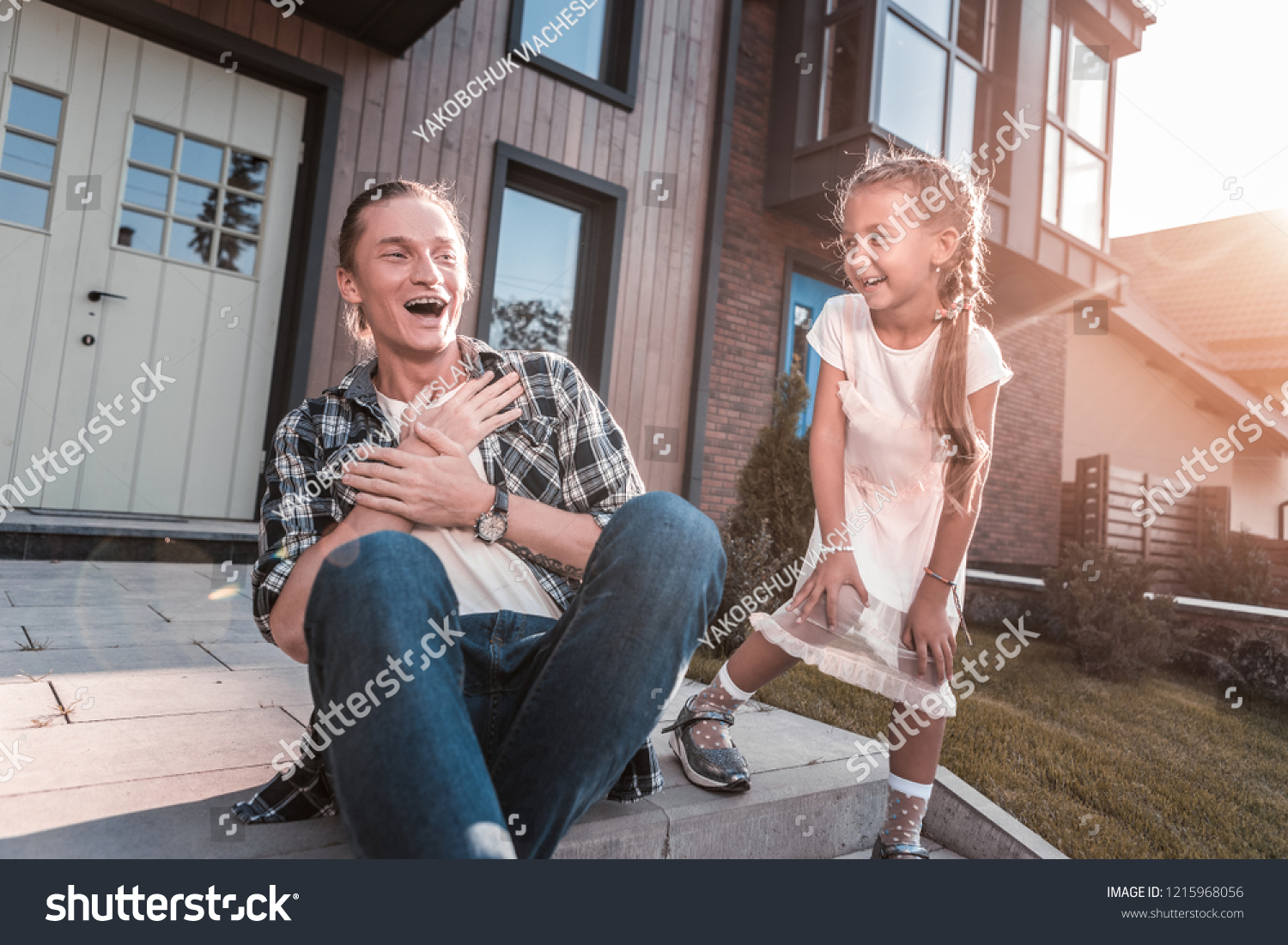 Beaming family. Beaming handsome father and cute daughter laughing while having fun outside their house #1215968056