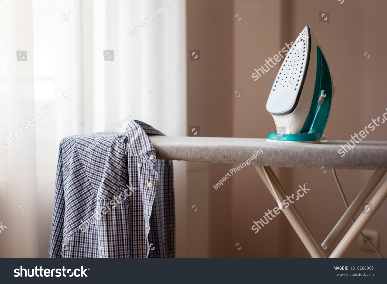 Ironed shirt hanging from an ironing board next to a hot iron. Selective focus on the iron #1216288969