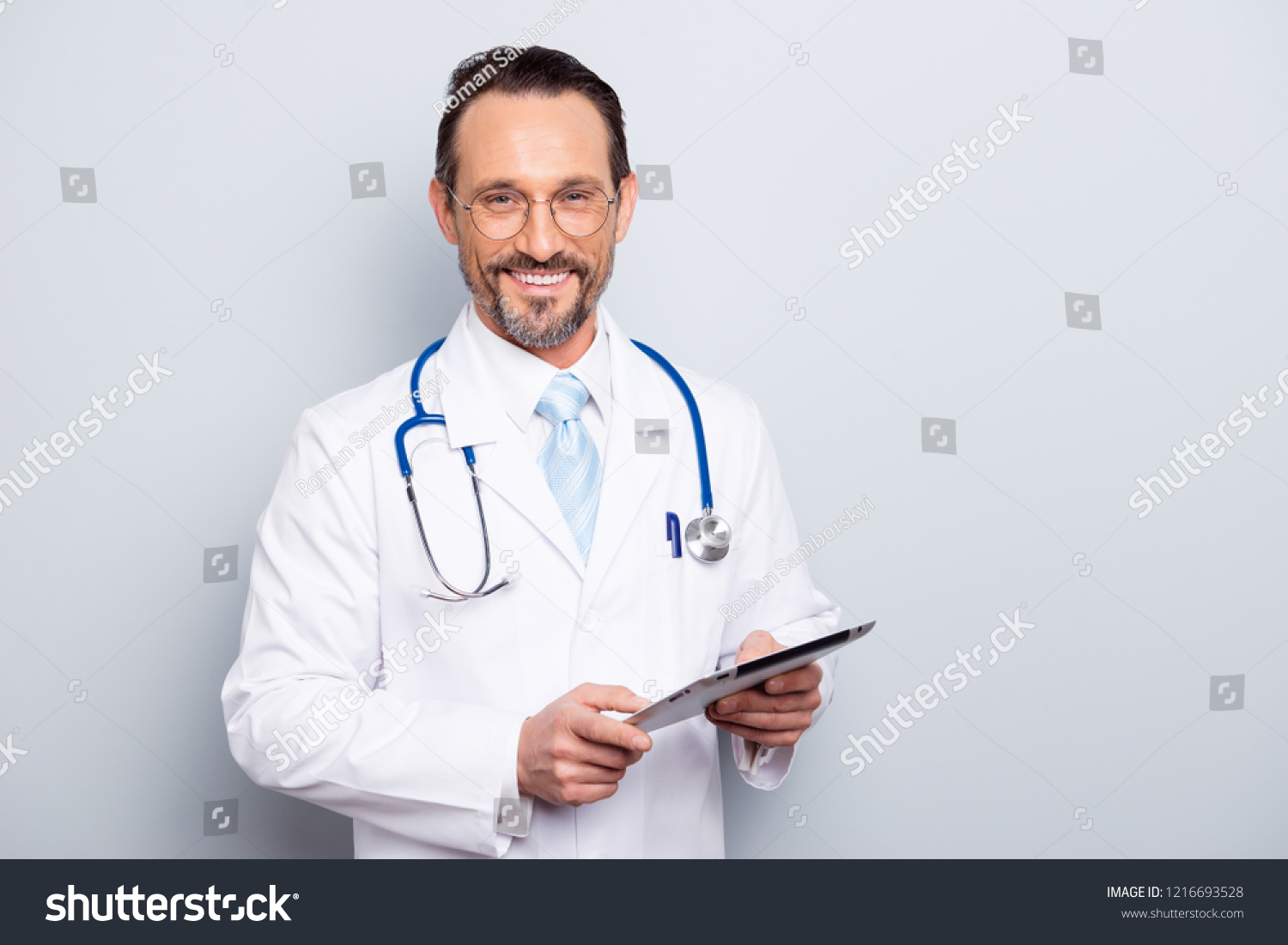 Portrait of half turn brunet hair bristle pharmacist man look at camera stand isolated on light gray background half turn make beaming toothy smile hold tablet in hands #1216693528