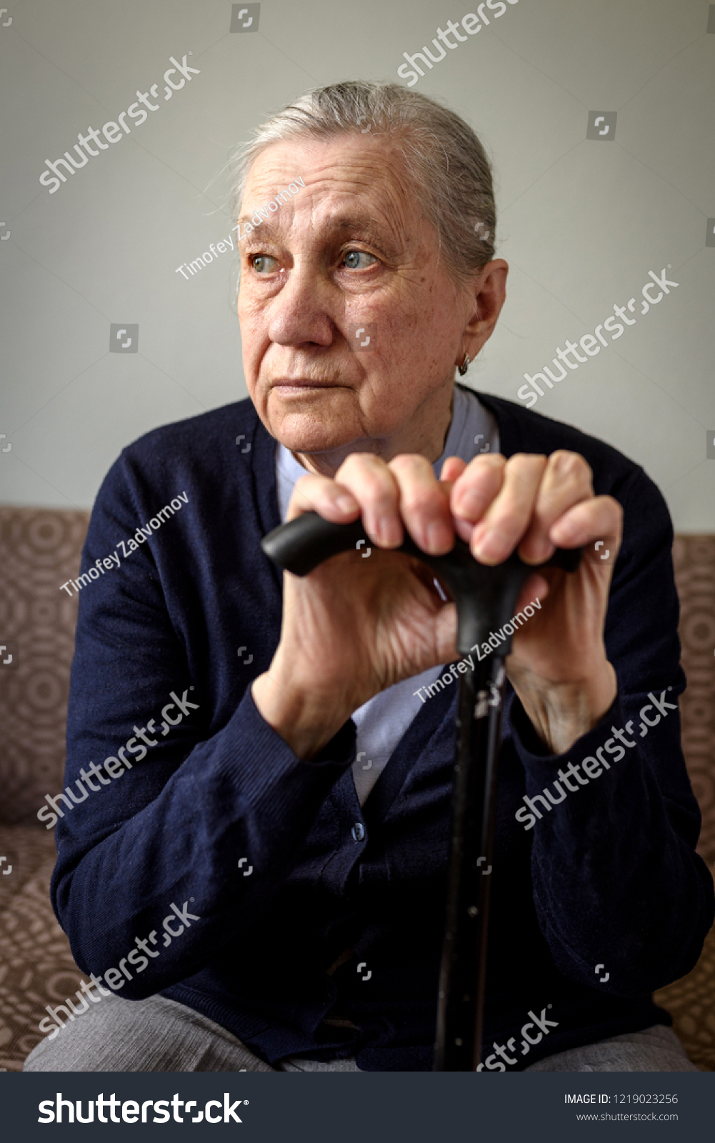 Sad old woman with a cane sitting on the couch. Old age, loneliness, health problems, memory problems. #1219023256