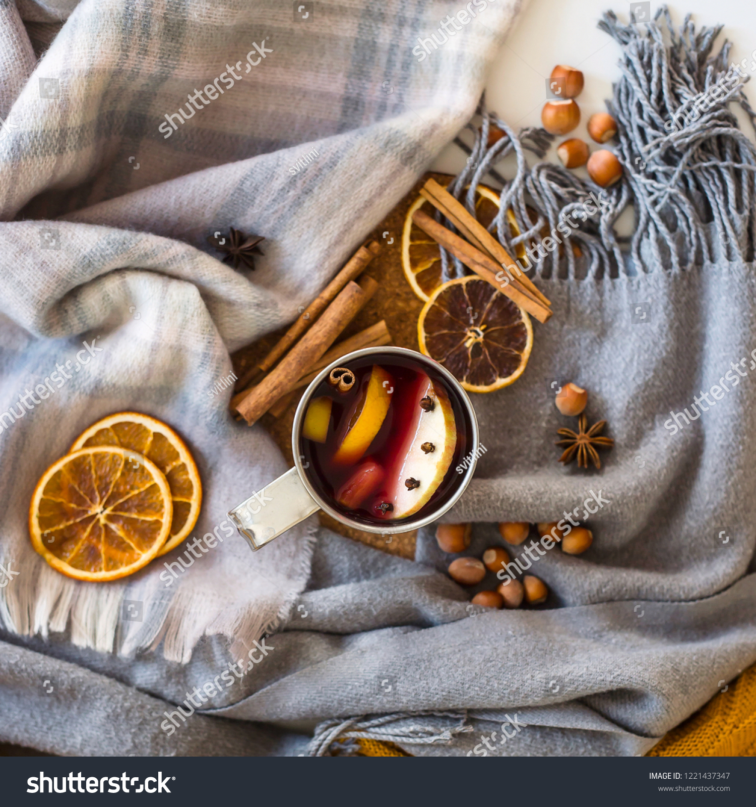 Mulled wine with apple, orange, clove, cinnamon and anise in a metal mug among winter plaids, scarves and sweaters. Hot drink on the eve Christmas eve #1221437347