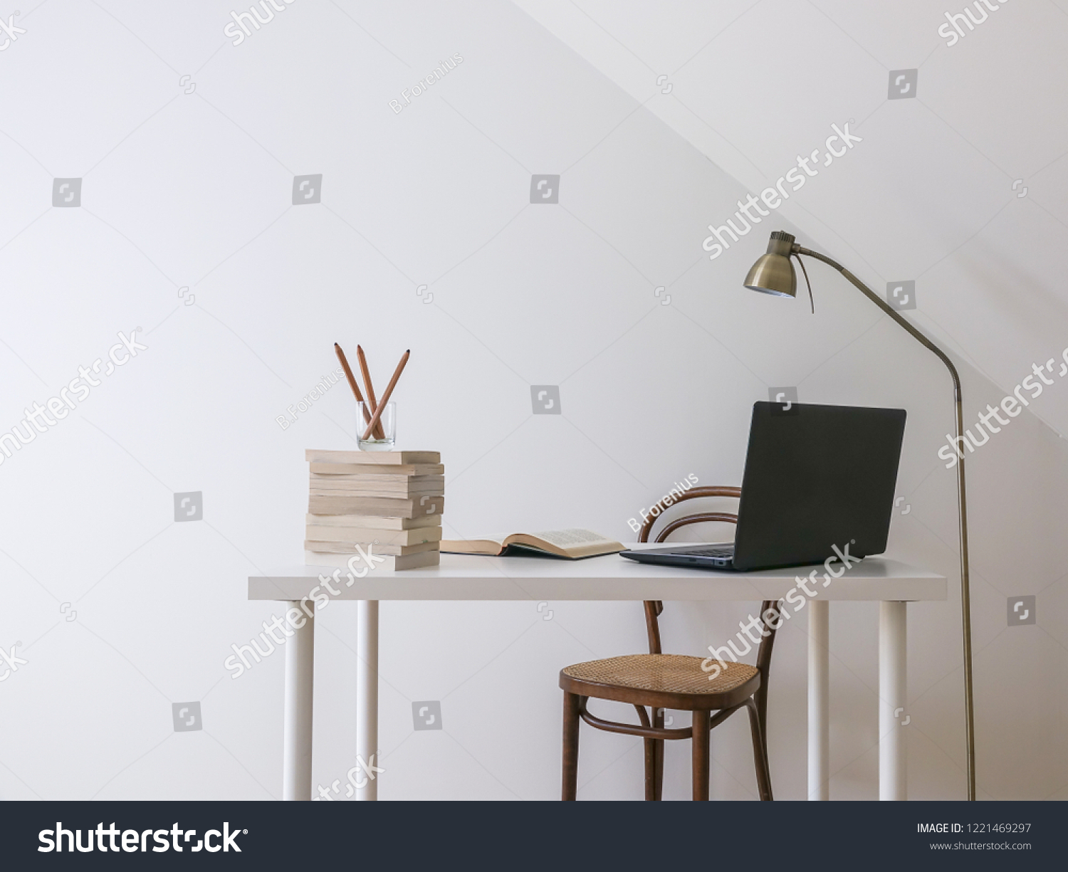 Simple workspace interior. Laptop computer, open book and a pile of books on a white modern desk. Empty white wall for copy space. #1221469297