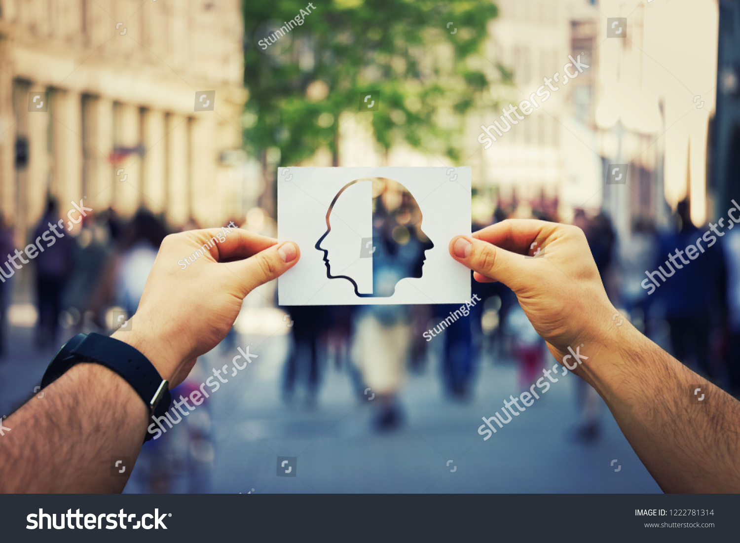 Man hands holding a white paper sheet with two faced head over a crowded street background. Split personality, bipolar mental health disorder concept. Schizophrenia psychiatric disease. #1222781314