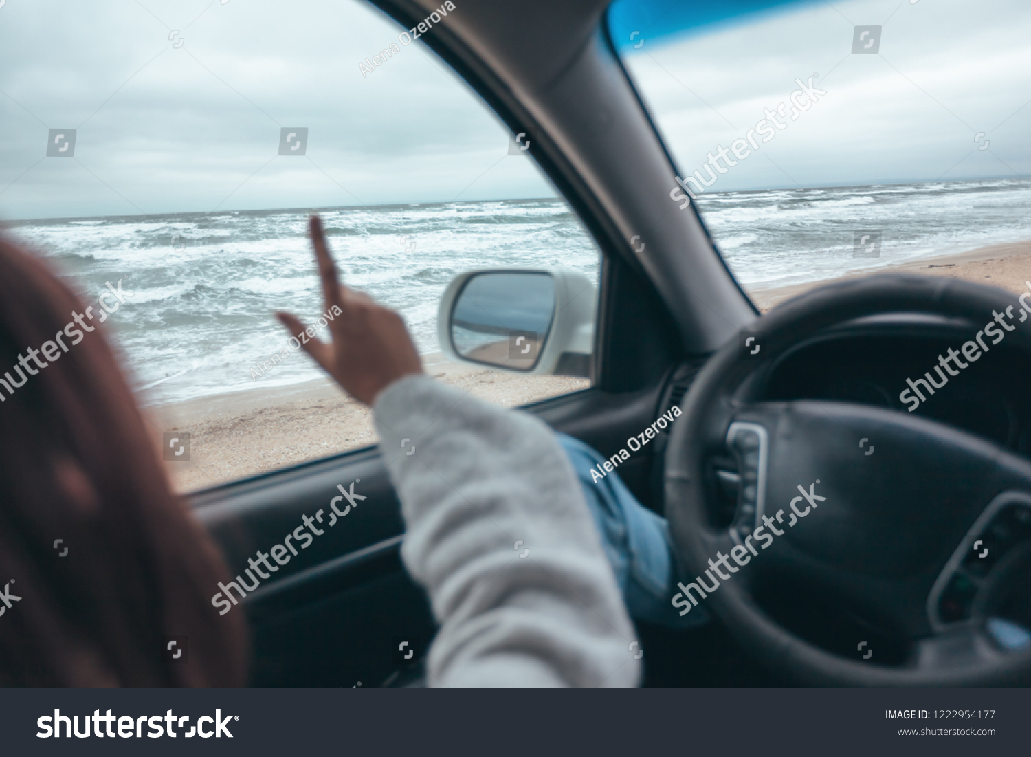 Young girl relaxing in car and looking at sea waves outside. Weekend trip in bad rainy weather. Dramatic winter travel concept. #1222954177