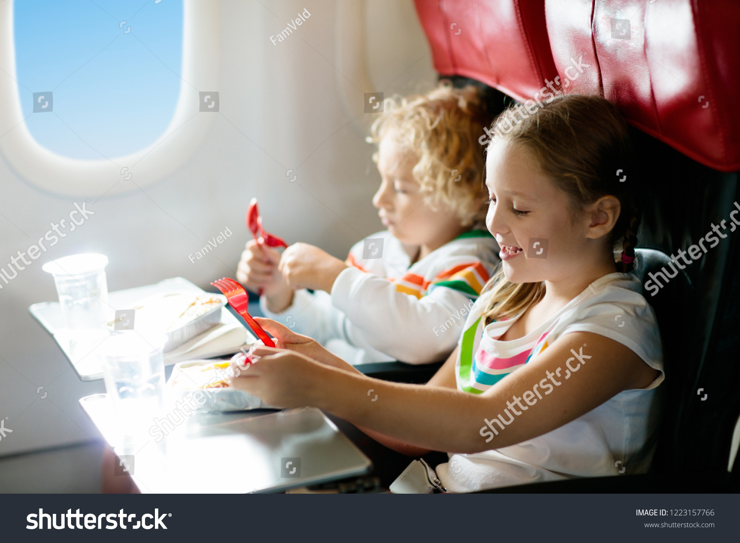 Child in airplane window seat. Kids flight meal. Children fly. Special inflight menu, food and drink for baby and kid. Girl and boy eating healthy lunch in airplane. Travel and family vacation.   #1223157766
