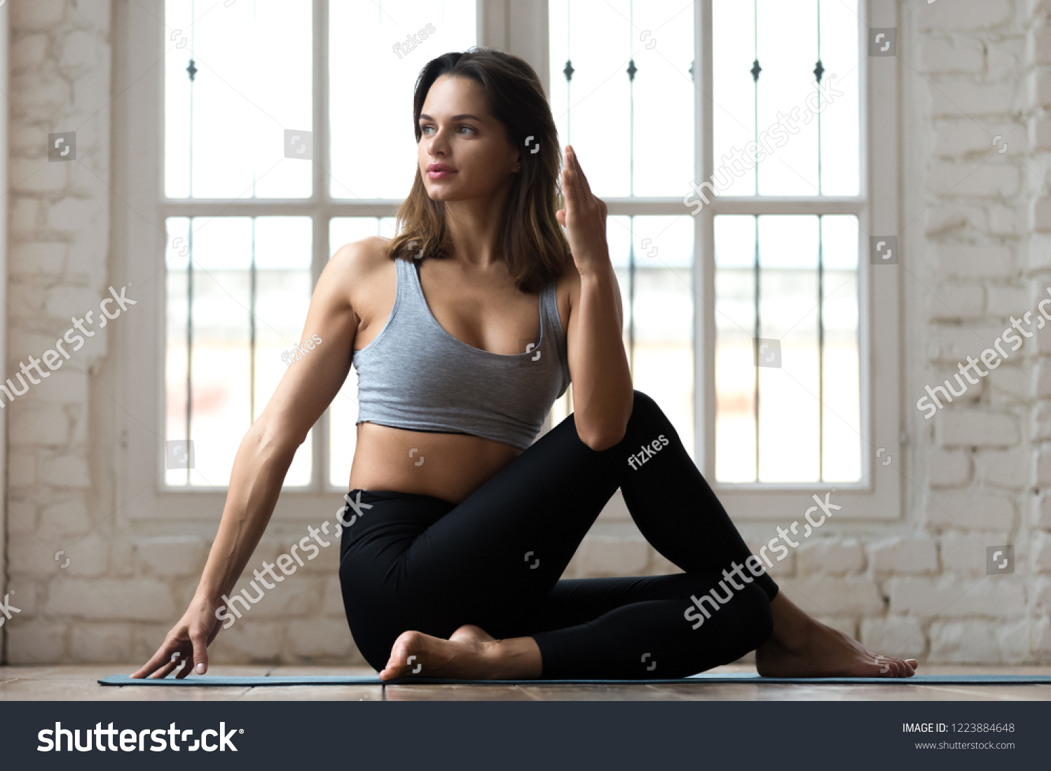 Young sporty attractive woman practicing yoga, doing Half lord of the fishes exercise, Ardha Matsyendrasana pose, working out, wearing sportswear, pants and top, indoor full length, white yoga studio #1223884648