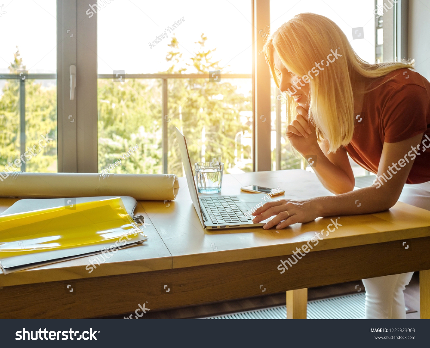 Searching for fresh ideas. Full length of young woman using computer while standing in the creative office near the window in sunny day. #1223923003