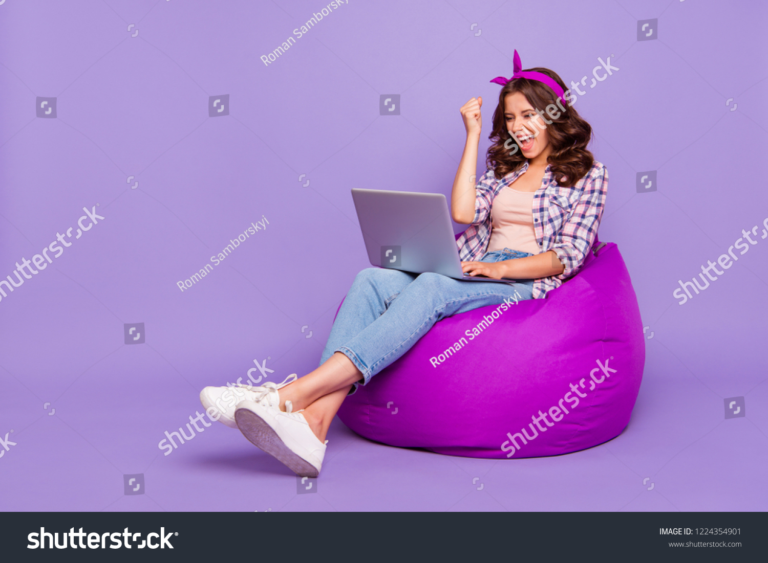 Full size portrait of lady in checkered shirt denim jeans her brunette curly wave style stylish hair she sit isolated on violet purple trendy background work on notebook open mouth raised fist up #1224354901