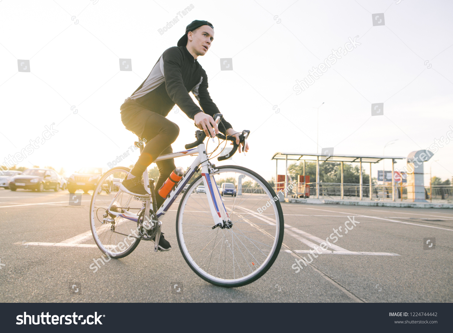 Portrait of an attractive cyclist in motion. Young rider in dark bike wears a bike on a street background and sunshine in the sunset. #1224744442