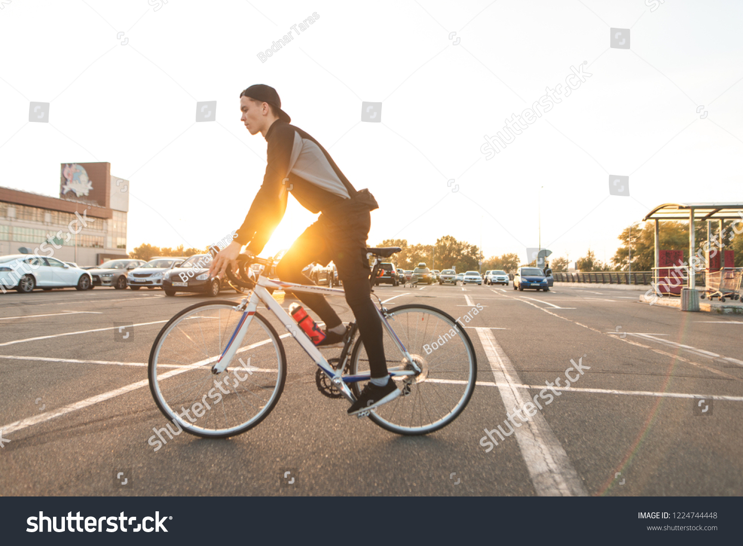 Portrait of an attractive cyclist in motion. Young rider in dark bike wears a bike on a street background and sunshine in the sunset. #1224744448