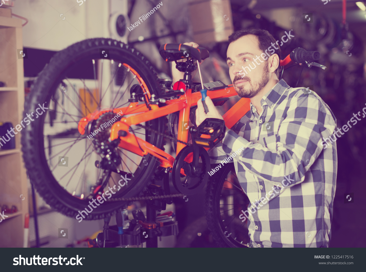 happy spanish man in sports workshop mounts bike using special tools #1225417516