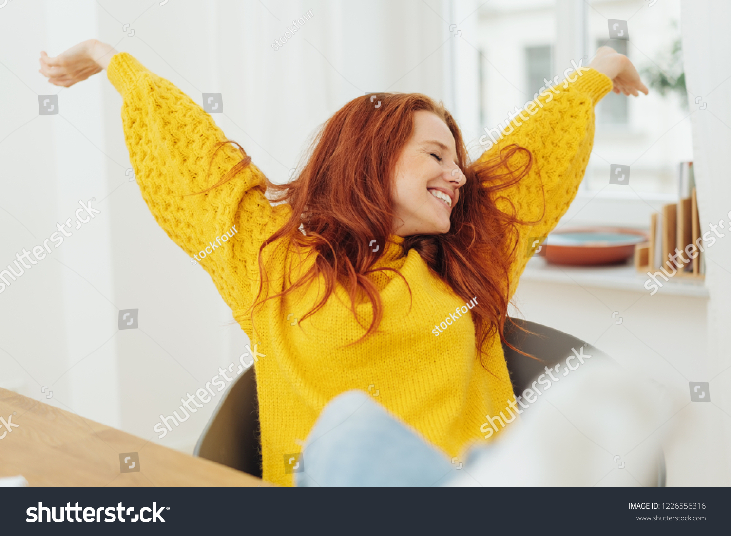 Happy pretty young woman stretching her arms as she leans back relaxing in her chair with a beaming smile #1226556316