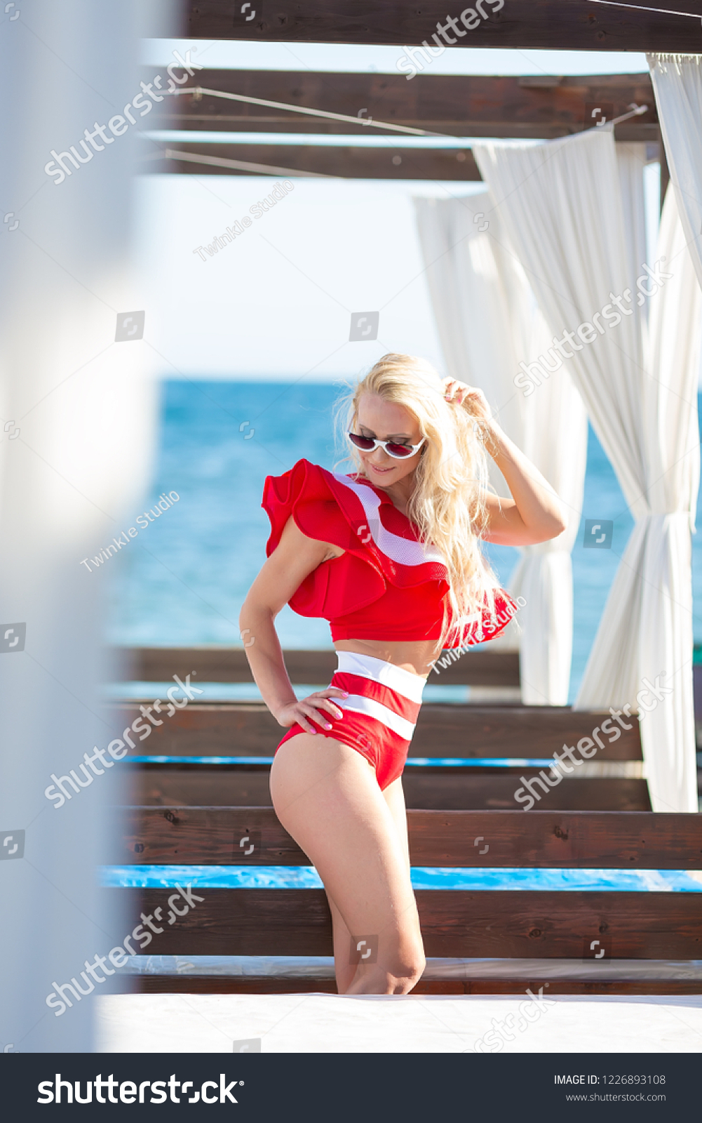 Sexy bikini body woman sun tanning relaxing on perfect tropical beach and turquoise ocean water. Sensual Seducing lady model walking in fashion red swimwear with smooth tanned skin and long lean legs #1226893108