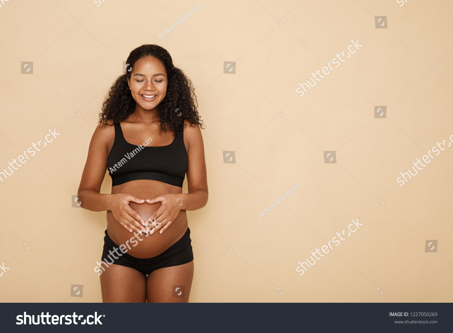 Pregnant woman holding hands on her belly making a heart symbol #1227050269