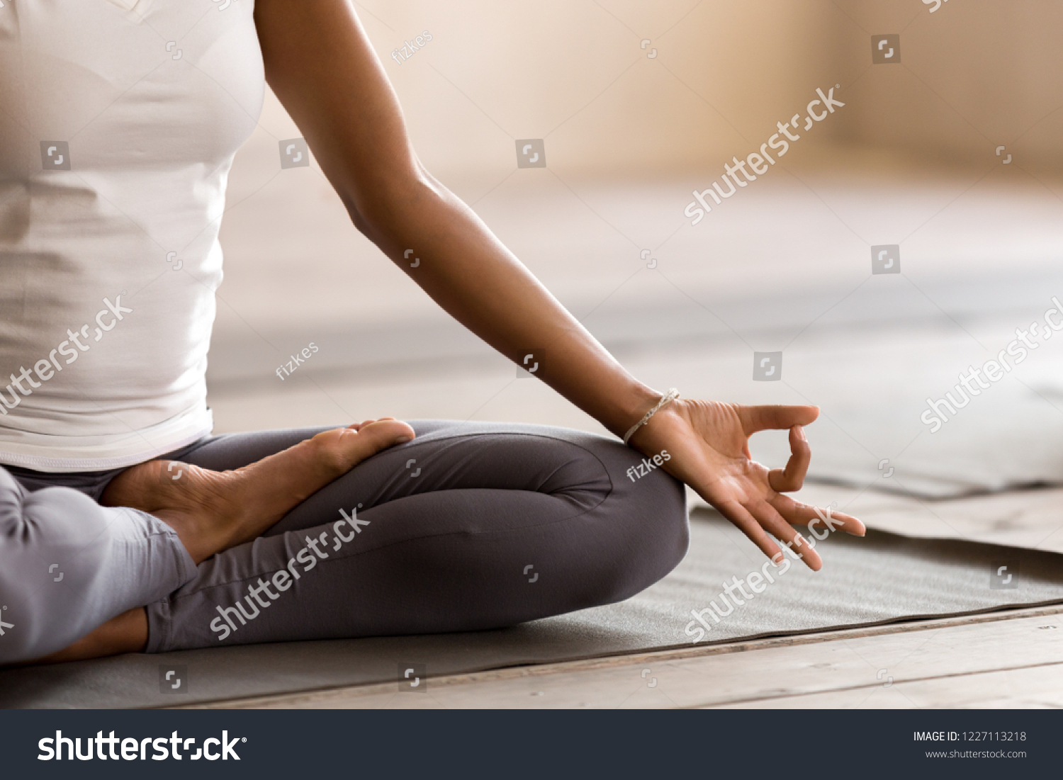 Yogi black woman practicing yoga lesson, breathing, meditating, doing Ardha Padmasana exercise, Half Lotus pose with mudra gesture, working out, indoor close up. Well being, wellness concept #1227113218