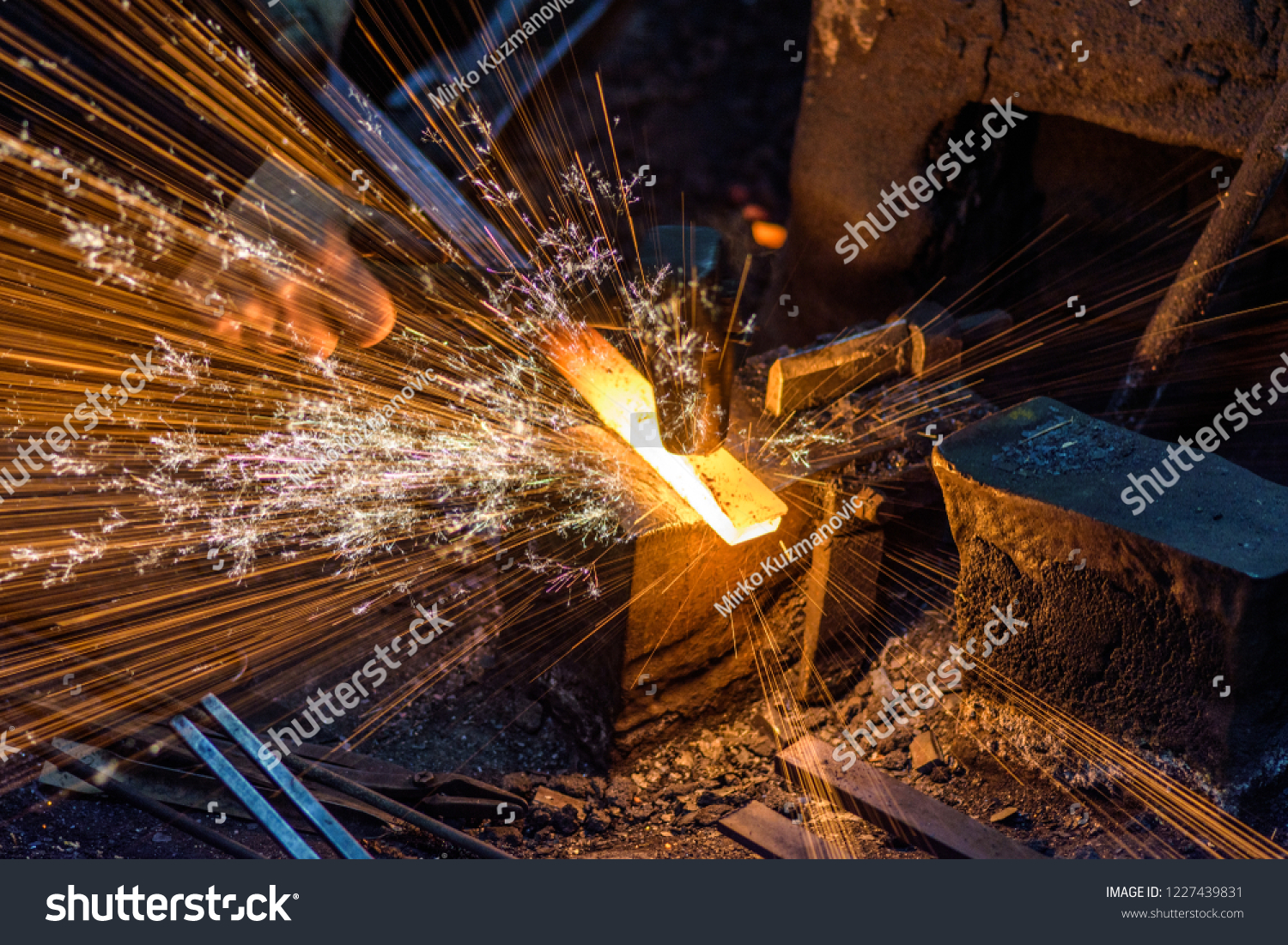 Blacksmith manually forging the molten metal on the anvil with spark fireworks #1227439831
