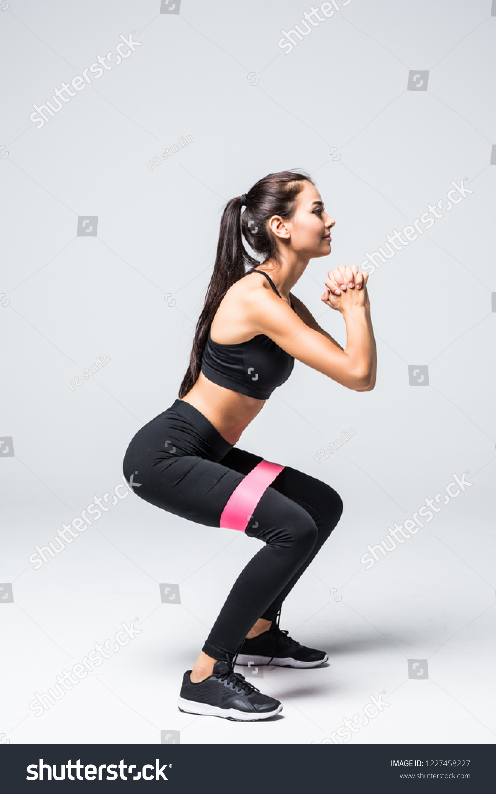 slim blonde woman doing squats with fitness loop band isolated on white background #1227458227